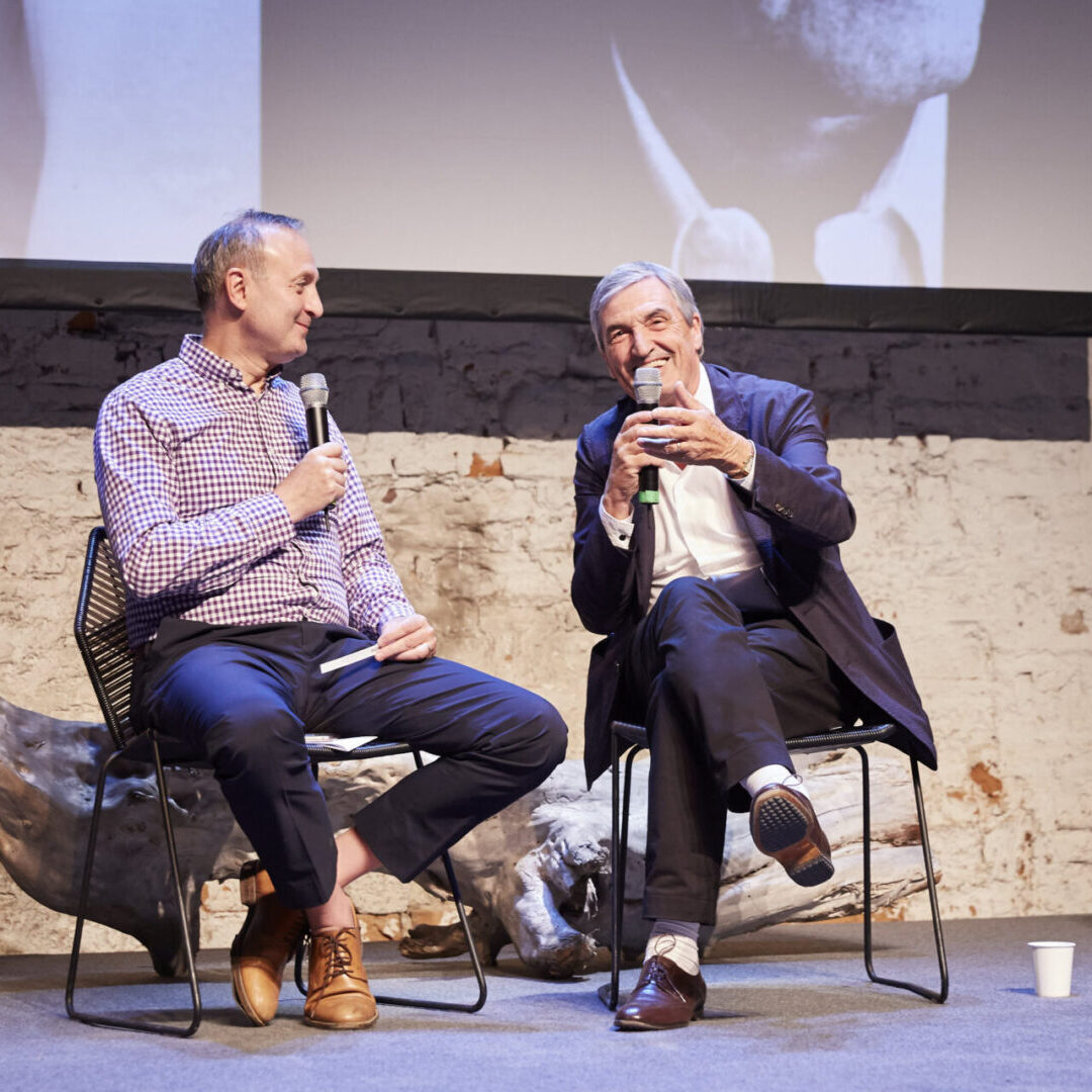 Two men sitting on chairs talking to each other.