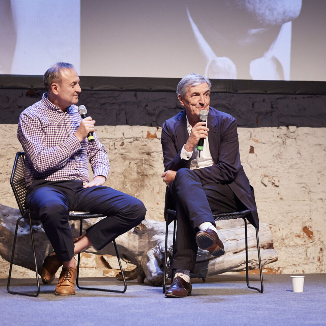 Two men sitting on chairs talking to each other.