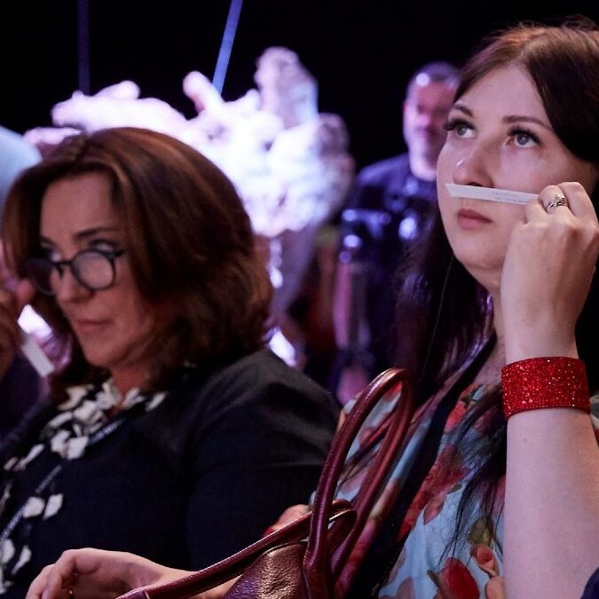 Two women are sitting in a room and one is holding a phone.
